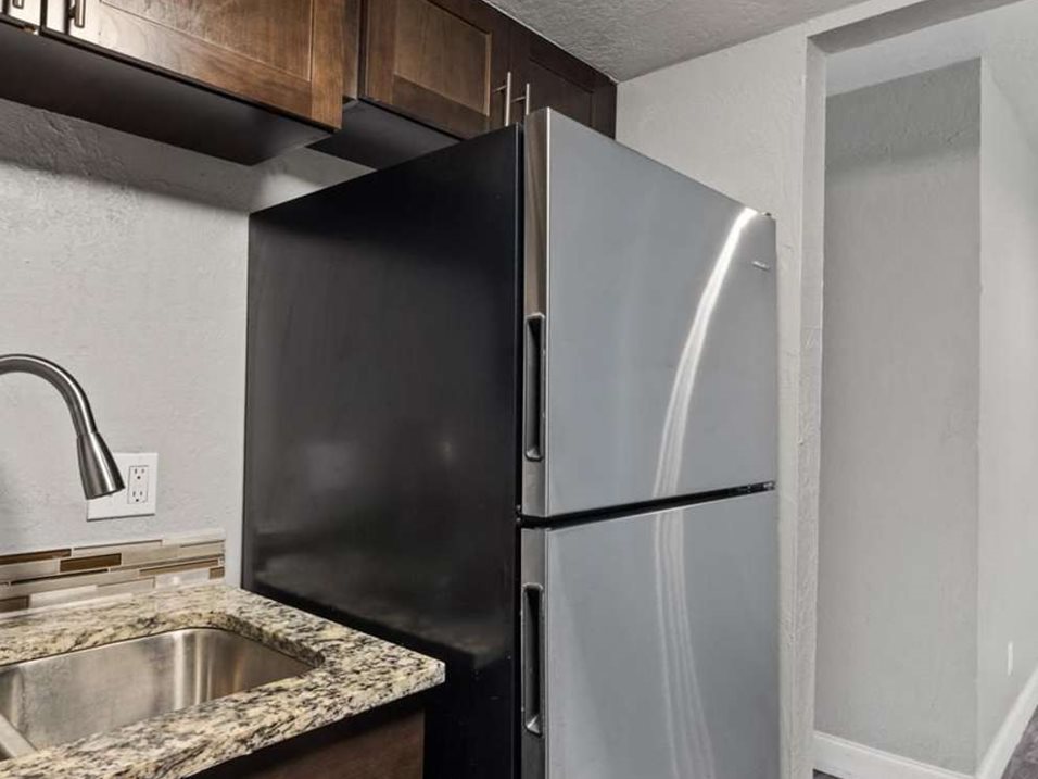 A black refrigerator in a kitchen with a granite countertop.